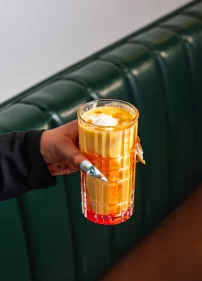 Hand holding a tall glass of creamy Mango Lassi topped with cream