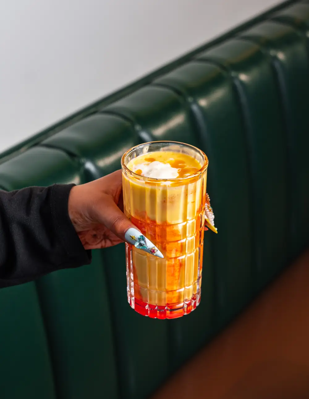 Hand holding a tall glass of creamy Mango Lassi topped with cream